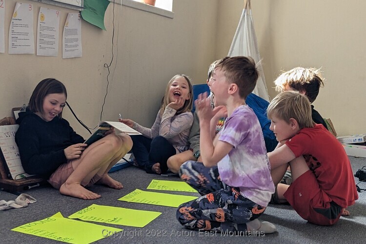 Learners at Acton Academy East Mountains outdoor-centric private school near Albuquerque, New Mexico engaged in a discussion together on the floor with big smiles on their faces. 