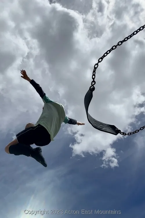 A learner flying through the air after jumping off the swing at Acton Academy.