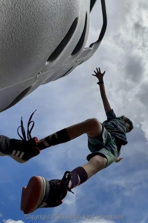 A learner suspended in the air blue sky and white clouds above at Acton Academy.