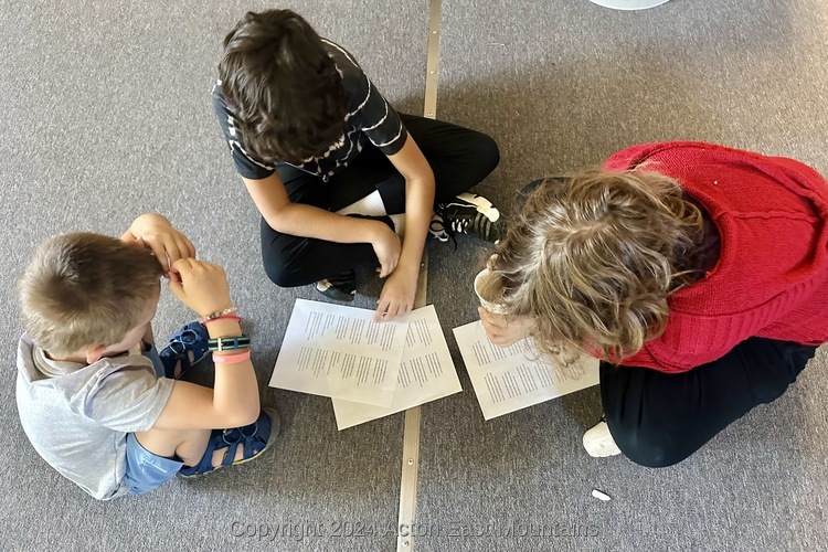 Learners at Acton Academy East Mountains private school sitting on the floor and reading papers. 